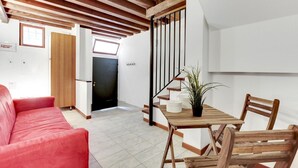 A room with a red sofa, wooden dining table, and chairs. There is a staircase with a metal railing leading to another room.