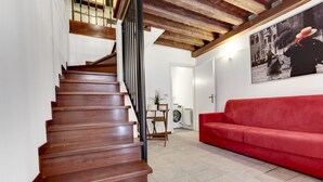A wooden staircase leading to a landing, a red sofa, and a black and white photograph on the wall.