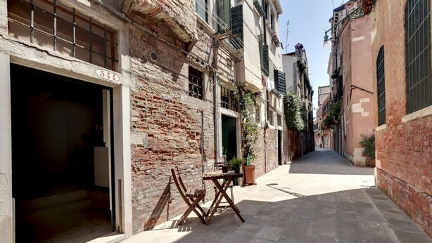 A narrow street with a building featuring a large open doorway and a small table with chairs outside.