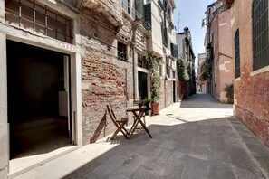Una calle estrecha con un edificio que tiene un amplio acceso abierto y una pequeña mesa con sillas afuera.