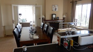 A dining area with a wooden table, black chairs, and a kitchen area with a toaster and a clock on the wall. - Fantastic Villa Amare on top of the Montemar (Benissa)