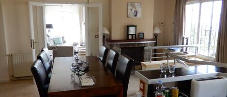 A dining area with a wooden table, black chairs, and a kitchen area with a toaster and a clock on the wall.