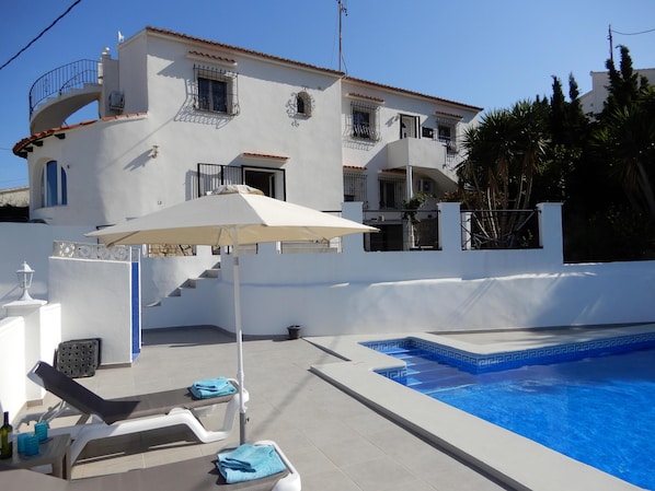Un bâtiment blanc doté d’une piscine, d’un espace extérieur aménagé et d’une zone couverte avec un parasol.