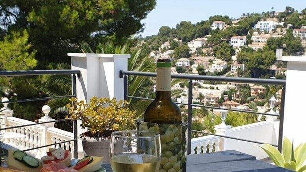 An outdoor dining area with a table set for a meal, including plates of food, a bottle of wine, and a glass of white wine. - Fantastic Villa Amare on top of the Montemar (Benissa)