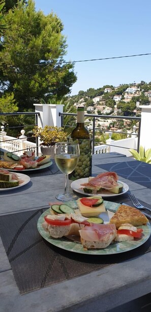 Un espace de restauration en plein air avec une table dressée pour un repas, comprenant des assiettes de nourriture, une bouteille de vin et un verre de vin blanc.