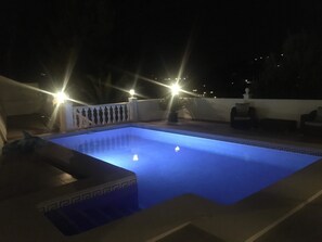 Une piscine à l’eau d’un bleu cristallin, entourée d’une terrasse blanche et d’un petit muret blanc.