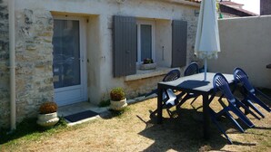 A stone building with a tiled roof, a covered outdoor seating area with chairs and an umbrella, and a small garden with potted plants. - studio - ST PIERRE D OLERON (Saint-Pierre-D'oléron)