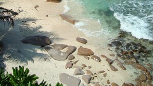 A beach with clear turquoise water, rocky outcrops, and a palm tree.
