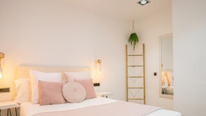 Een keurig opgeruimde slaapkamer met een groot bed, nachtkastjes, een spiegel en een hangende plant.