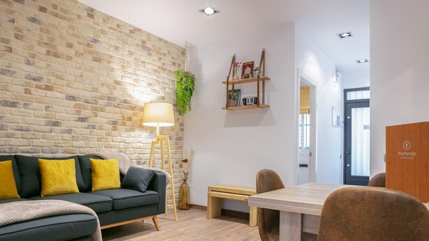 Een moderne woonkamer met een bakstenen muur, een bank met gele kussens, een houten bijzettafeltje en een lamp.