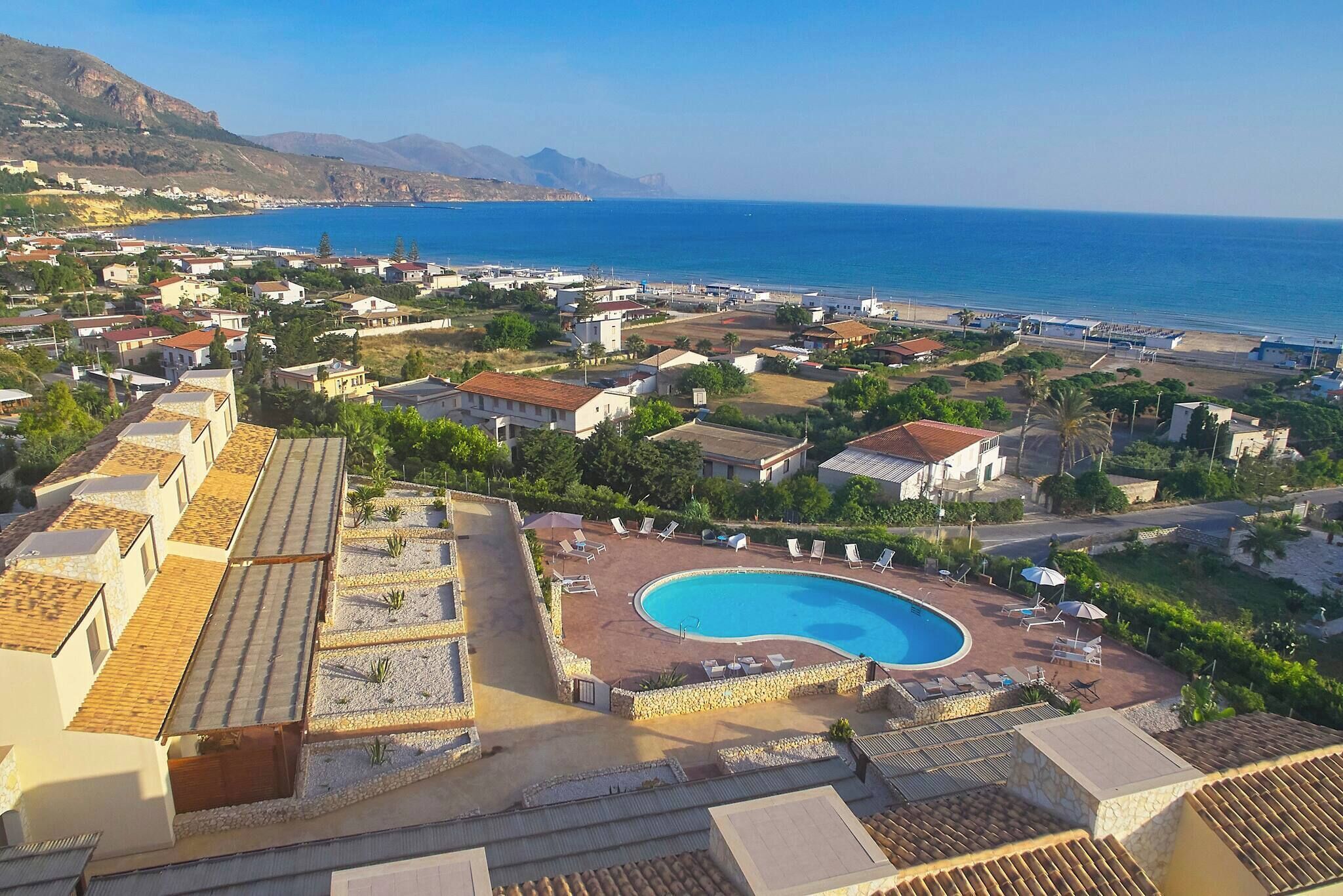 Un complejo turístico frente al mar, con piscina, playa y montañas al fondo.