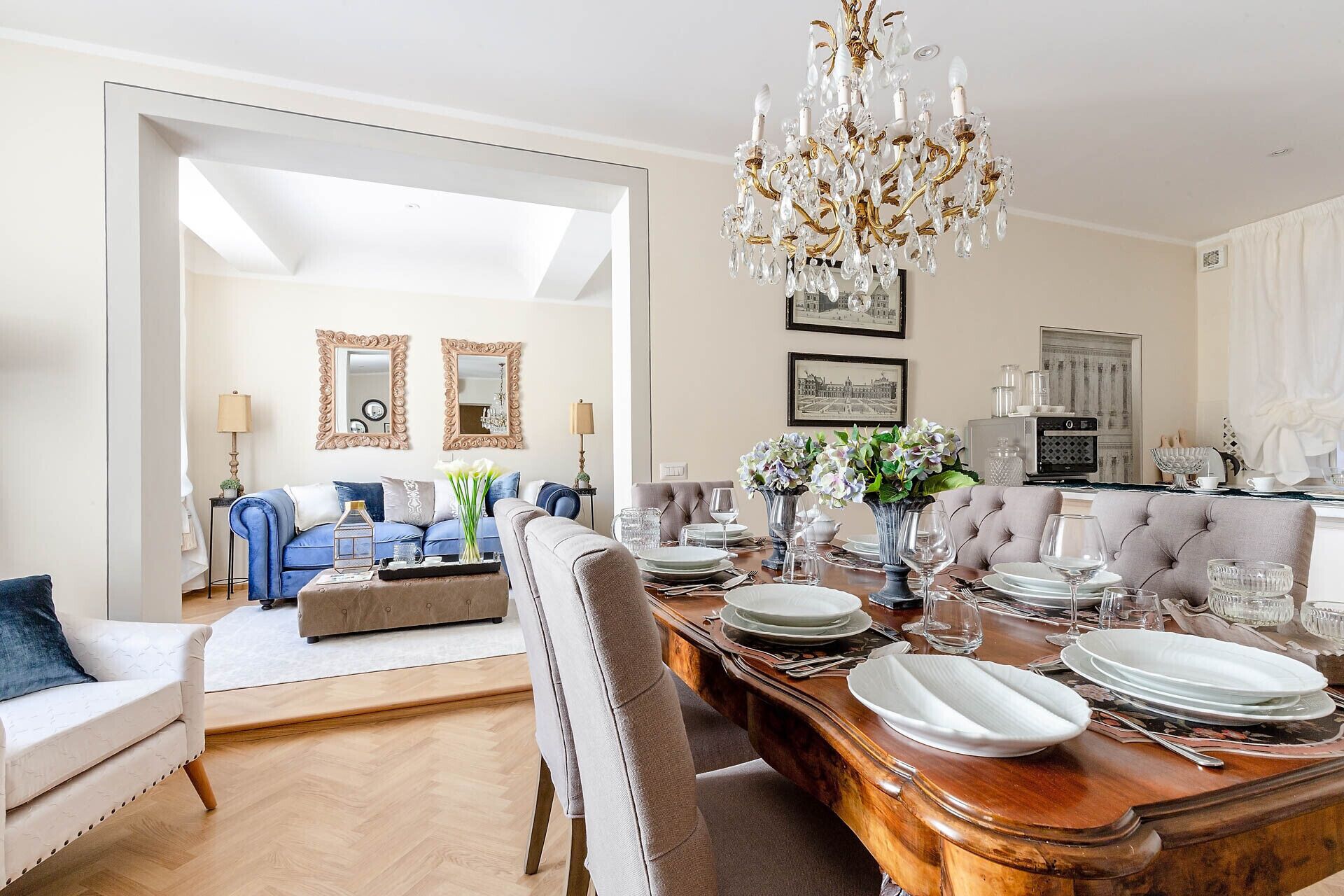 A dining area with a wooden table set for a meal, a chandelier, and a sofa in the background.