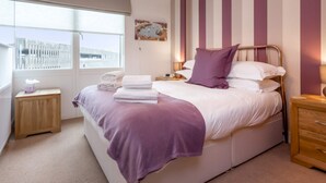 A bedroom with a bed, a nightstand, a bedside table, a window, and a view of the outside.