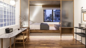 Quarto moderno com cama, escrivaninha e cadeira. Há uma janela com vista para edifícios.