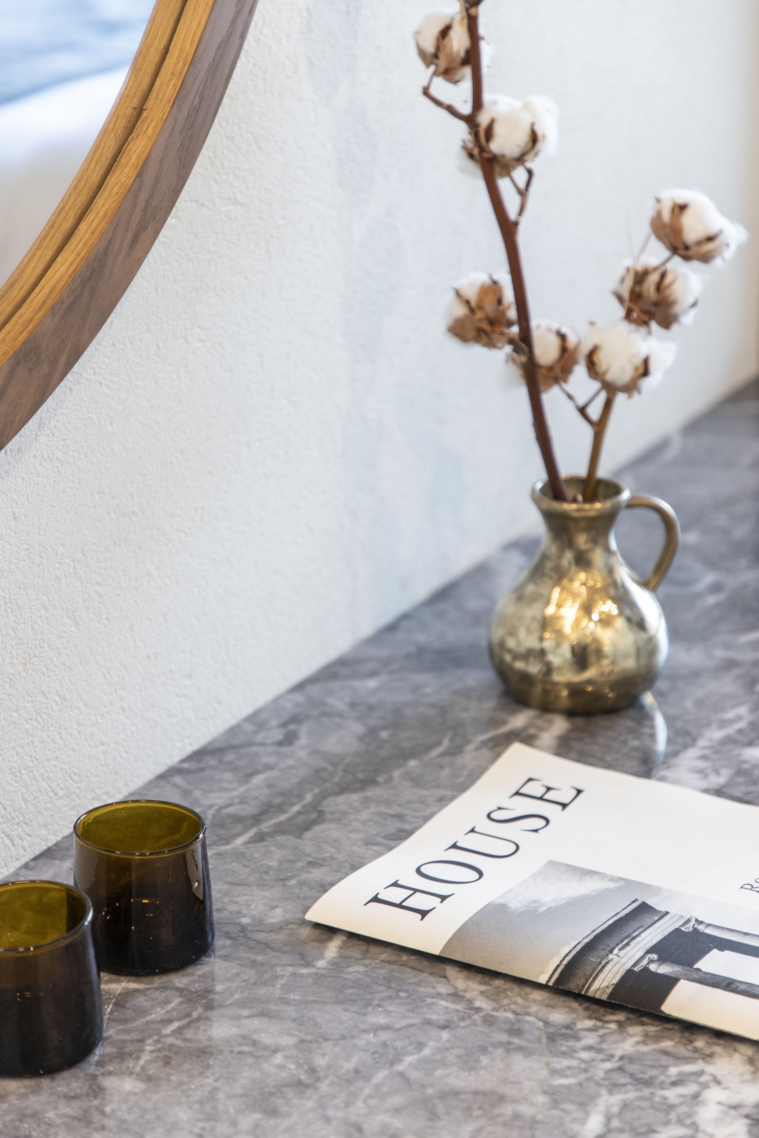 A marble countertop with a vase of cotton branches, two dark glasses, and a magazine titled "HOUSE".