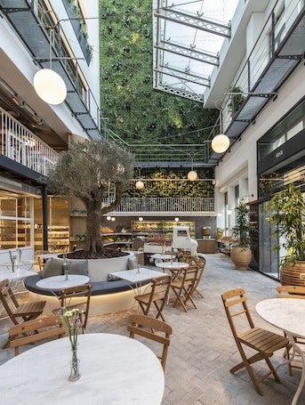 An indoor courtyard with tables and chairs, a central tree, and a food display.