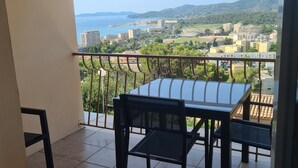 Un balcone con tavolo e sedie, vista su una cittadina costiera e montagne.