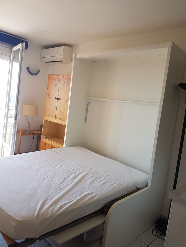 Een slaapkamer met een bed, een kledingkast, een bureau en een lamp.