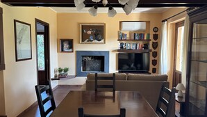 A dining area with a wooden table and chairs, a fireplace, a sofa, and a bookshelf with books and decorative items. - Villa Lucia, with an infinity pool and garden, in an oasis of peace  (Siracusa)
