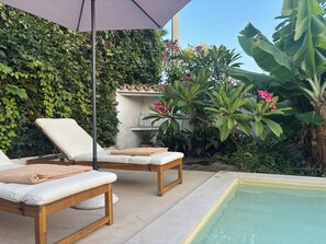 Zona de piscina amb dues gandules, una petita estàtua i vegetació exuberant.