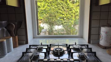 Een keuken met een gasfornuis, een raam met uitzicht op groen en keukengerei op het aanrecht.