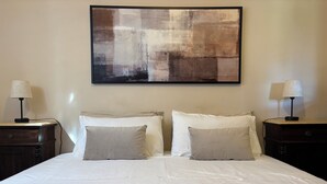 Ein Hotelzimmer mit einem großen Bett, zwei Nachttischen mit Lampen und einem großen abstrakten Gemälde an der Wand.