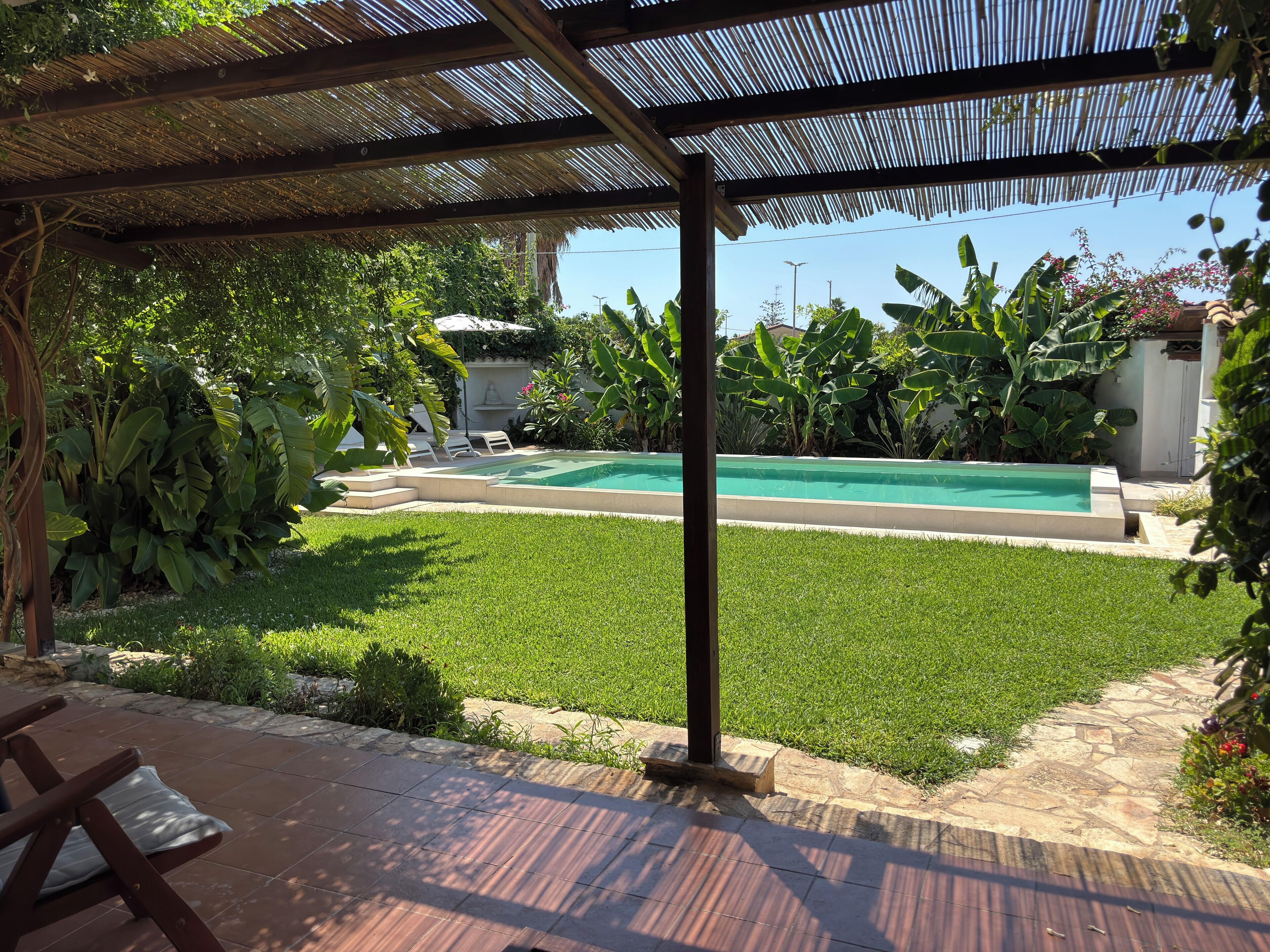 A backyard with a swimming pool, surrounded by lush greenery and a pergola.