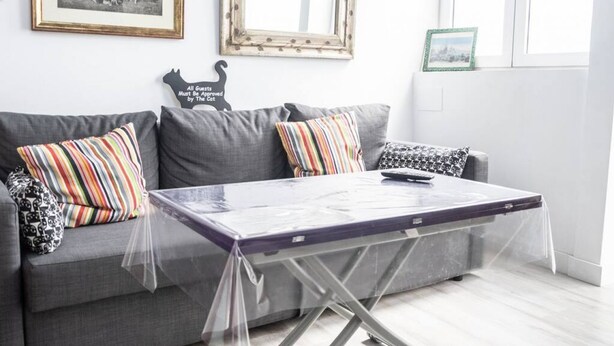 A living room with a grey sofa, striped pillows, a glass-top coffee table, and a framed picture on the wall.