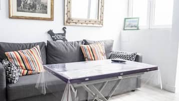 A living room with a grey sofa, striped pillows, a glass-top coffee table, and a framed picture on the wall.