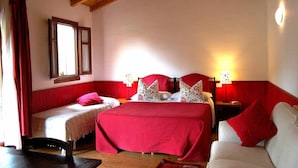 A room with two beds, a wooden ceiling, a window with red curtains, and a nightstand with a lamp.