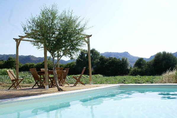 Un espace aménagé au bord de la piscine, avec une pergola, des chaises en bois et une table.