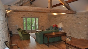 A rustic room with exposed wooden beams, a green sofa set, a wooden coffee table, and a patterned rug.