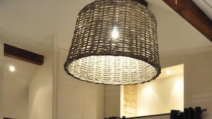 A room with a wicker ceiling light, a chair, a bed, and a view through a glass door.