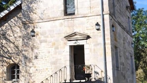 A stone building with a red door, a staircase, and a small window.