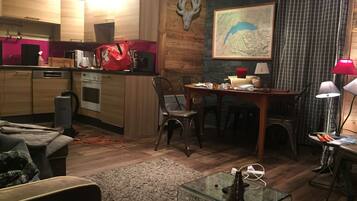 Een moderne keuken met houten kastjes, een eethoek met tafel en stoelen, een glazen salontafel en een opgehangen hertenthoorn aan de muur.