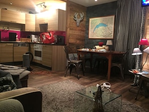 Een moderne keuken met houten kastjes, een eethoek met tafel en stoelen, een glazen salontafel en een opgehangen hertenthoorn aan de muur.