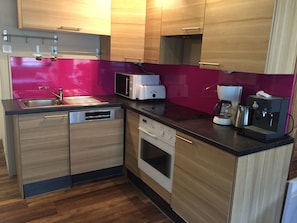 Een moderne keuken met houten kastjes, een magnetron, een broodrooster, een koffiezetapparaat en een vaatwasser.