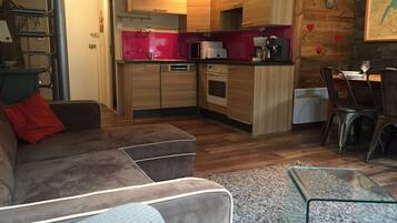 Een moderne keuken met houten kastjes, een rode achterwand en een eethoek met een glazen tafel en stoelen.