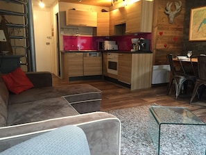 Een moderne keuken met houten kastjes, een rode achterwand en een eethoek met een glazen tafel en stoelen.