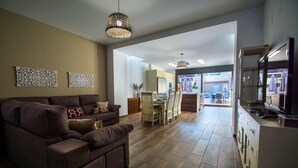 A modern living room with a brown sofa, dining area with chairs, and a kitchen with cabinets. - House with central pool, barbecue, wifi, a.a. and 300m from the beach. (Calella)