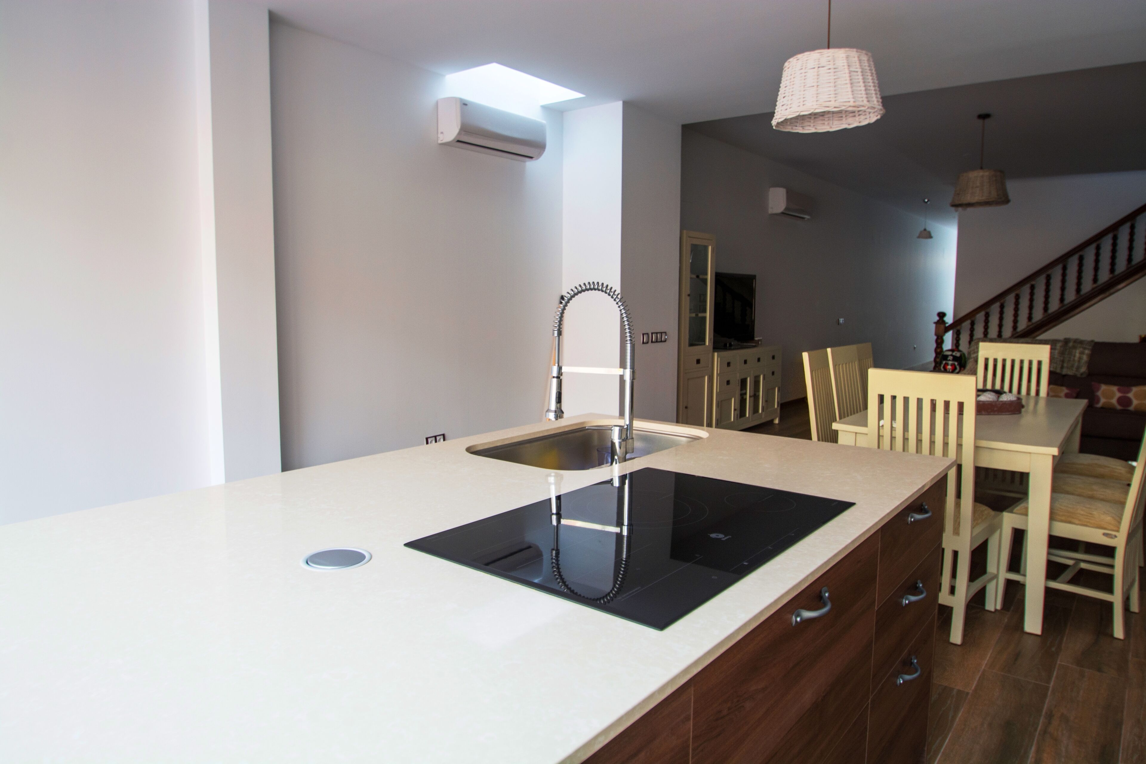 A modern kitchen with a built-in sink, a dining area with wooden chairs, and a staircase in the background.