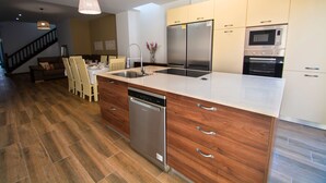 A modern kitchen with a dishwasher, stainless steel appliances, wooden cabinetry, and a dining area with chairs and a table. - House with central pool, barbecue, wifi, a.a. and 300m from the beach. (Calella)
