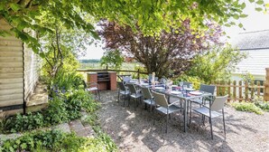 Eine Terrass mit Tisch und Stühlen, umgeben von einem Holzzaun und einem Baum, der Schatten spendet.