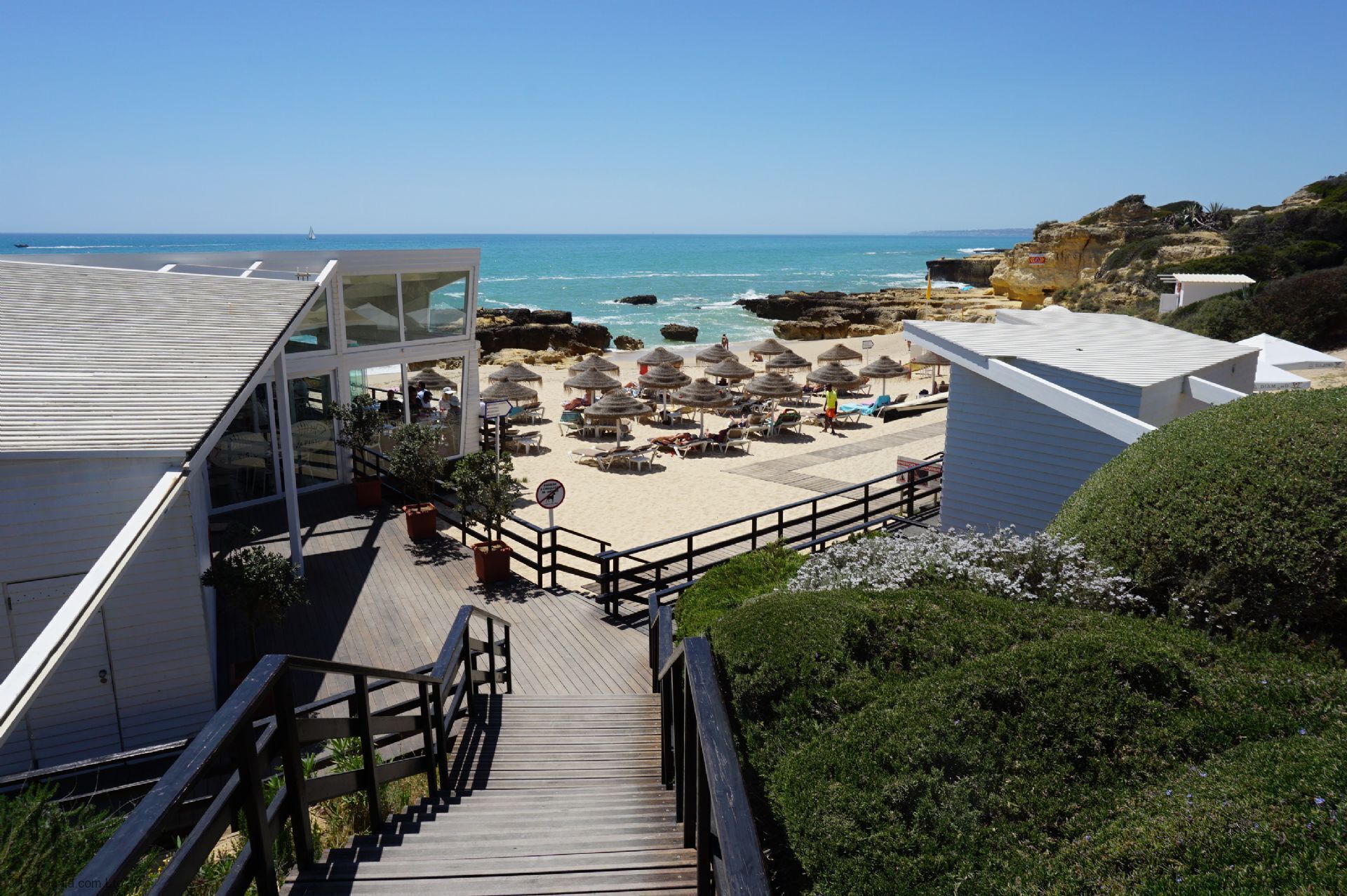 A beachside hotel with a wooden staircase leading to a deck with beach umbrellas and lounge chairs.