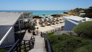 A beachside hotel with a wooden staircase leading to a deck with beach umbrellas and lounge chairs. - Villa Borboleta, Albufeira.  Quality Villa, Private Pool, Air Conditioning, 3 Bedrooms, 4 Bathrooms. (Albufeira)