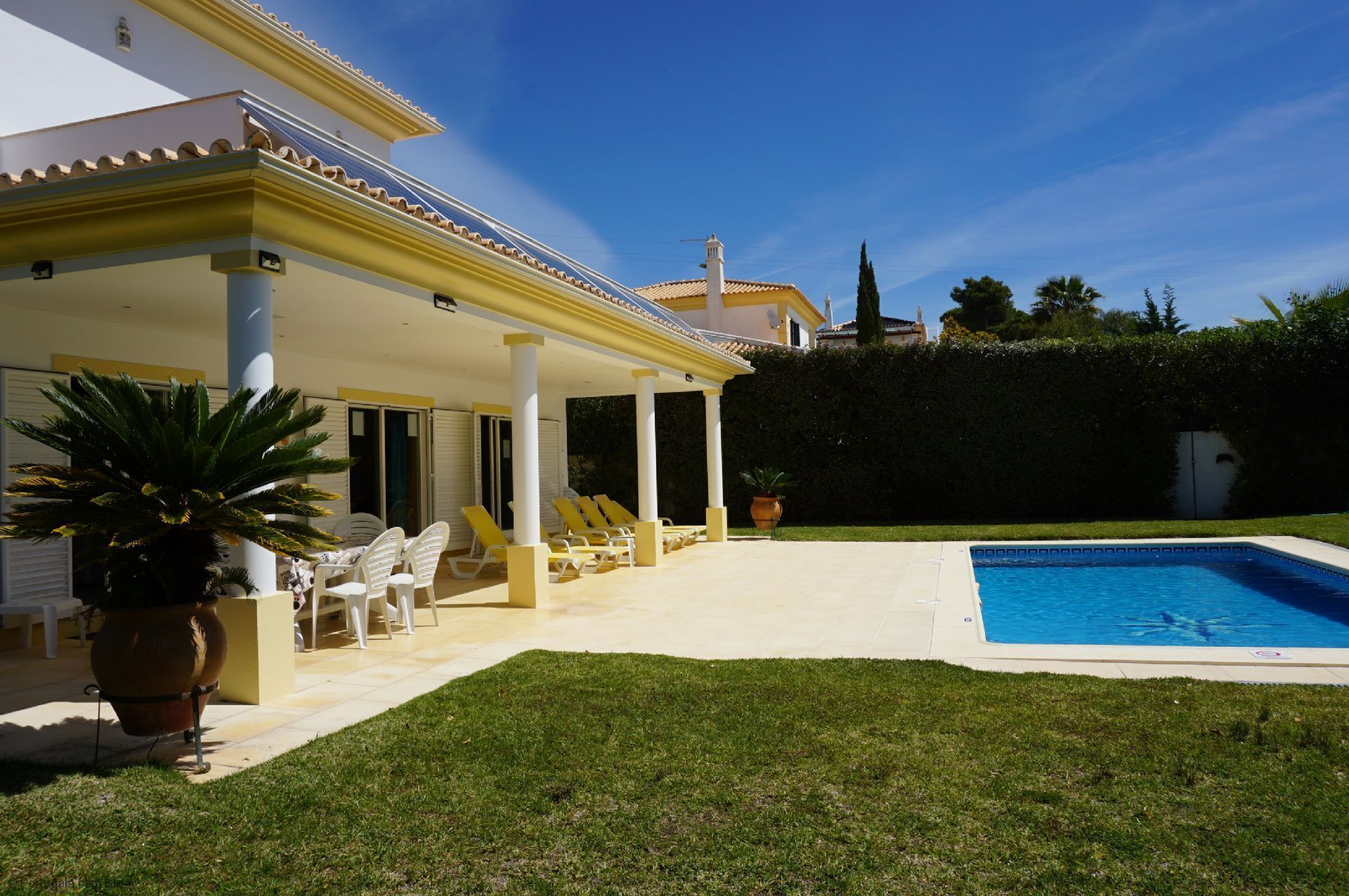 A poolside area with a covered patio, lounge chairs, and a swimming pool.