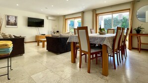 A spacious living area with a dining table and chairs, a sofa, and a television mounted on the wall. - Villa Borboleta, Albufeira.  Quality Villa, Private Pool, Air Conditioning, 3 Bedrooms, 4 Bathrooms. (Albufeira)