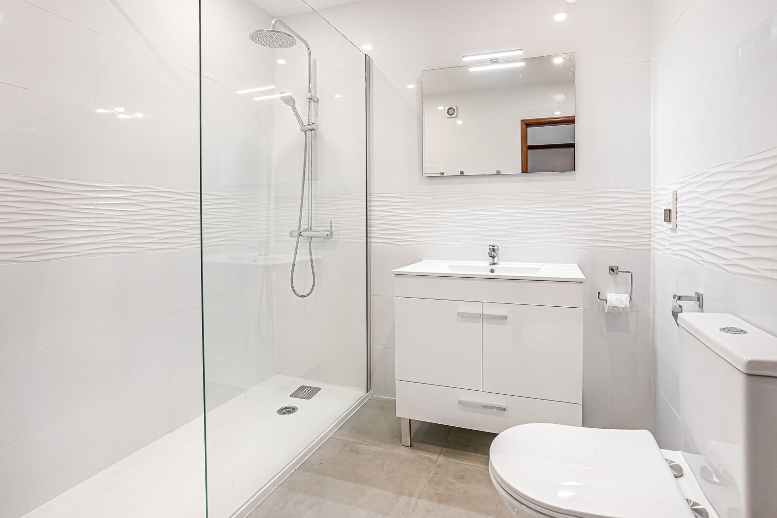 A modern bathroom with a glass-enclosed shower, a white sink, and a toilet.