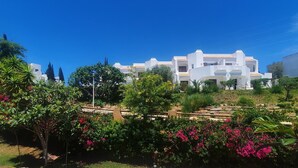 A white building with a tiled roof, surrounded by greenery and flowering plants. - Recently Renovated Ground Floor Apartment, 2 new Bathrooms with walk in showers  (Albufeira, Faro)