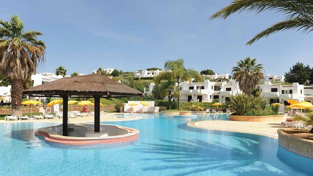 A swimming pool with a central gazebo, surrounded by lounge chairs and umbrellas, with white buildings in the background. - Recently Renovated Ground Floor Apartment, 2 new Bathrooms with walk in showers  (Albufeira, Faro)